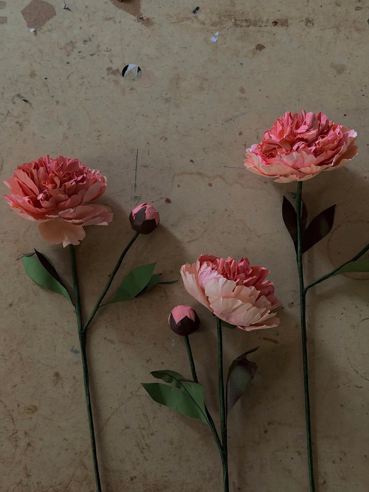 Three beeswax paper Chinese peony flower stems on a neutral surface