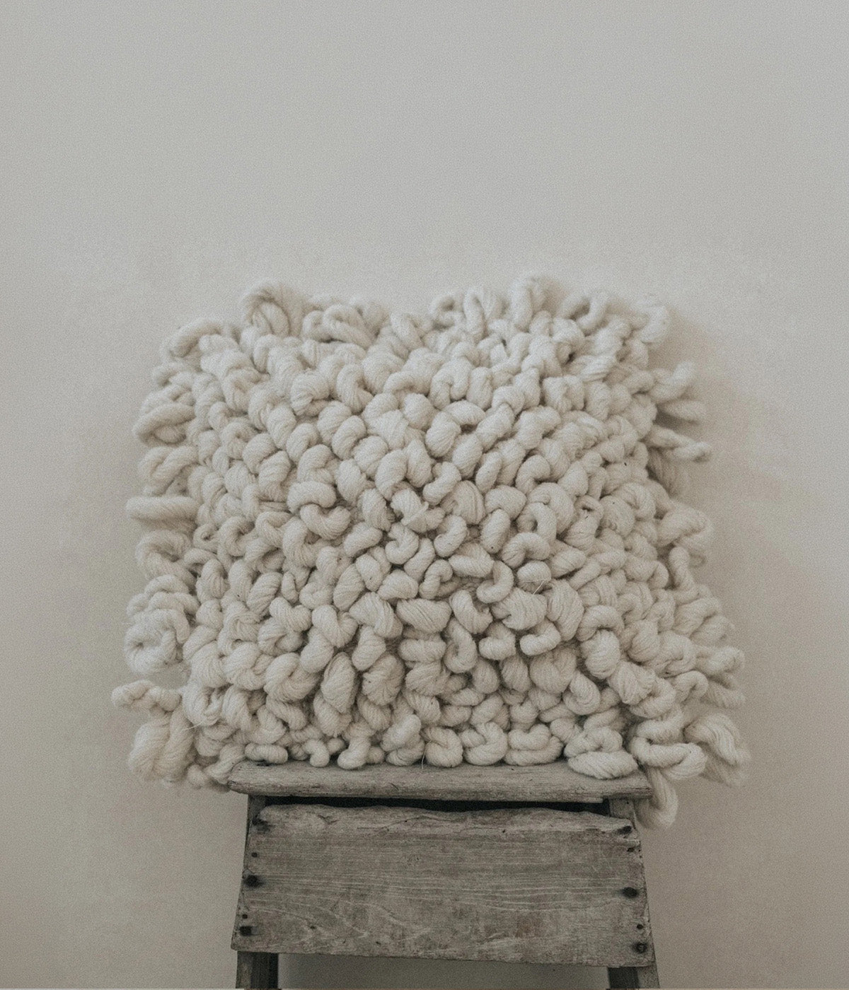 A chunky knit throw pillow in a warm off-white or cream color