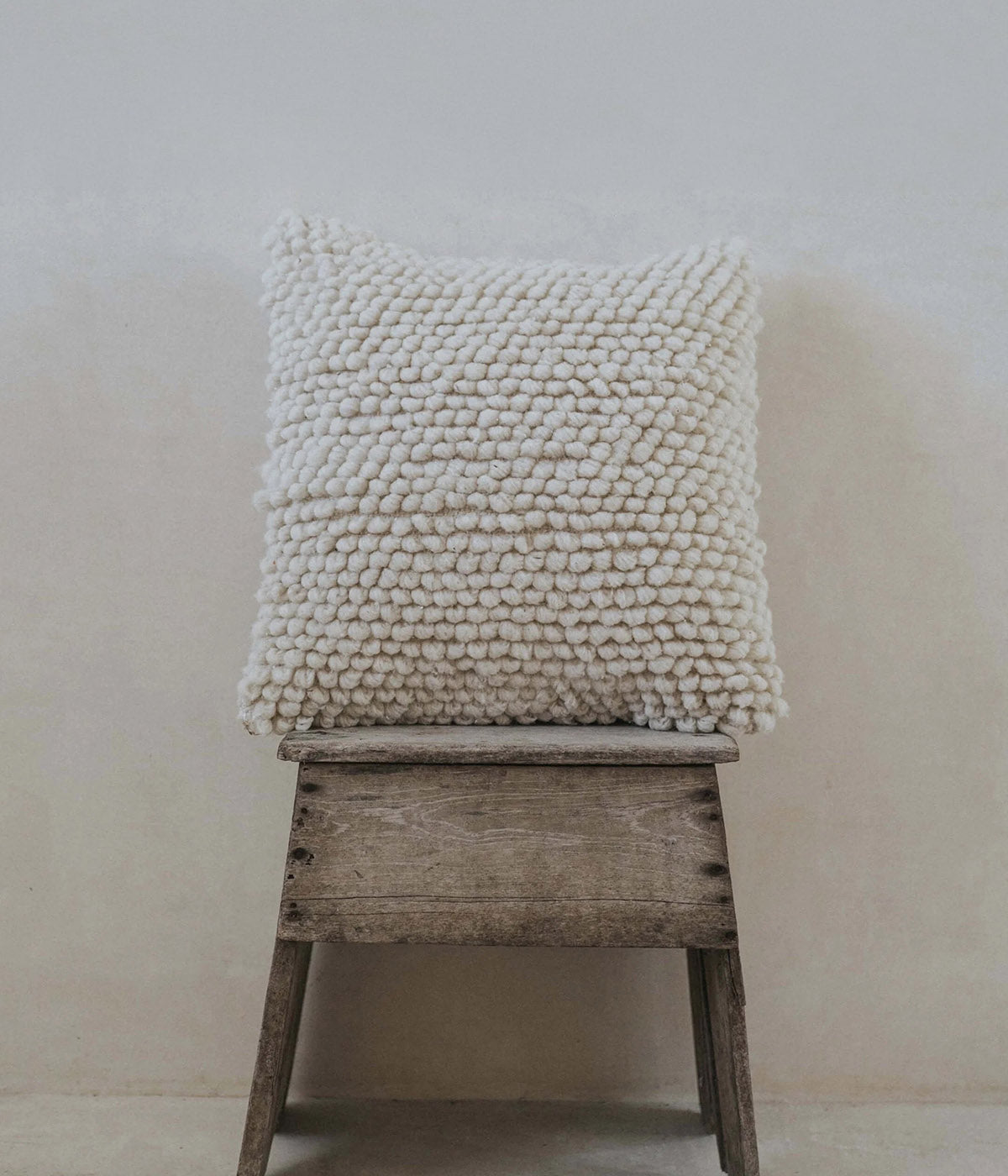 A square off-white textured throw pillow with a chunky, looped pom-pom style fabric